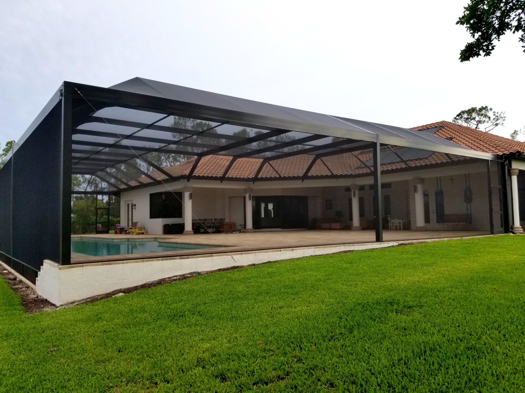 Large black aluminum screen enclosure beside a tile-roof Florida home
