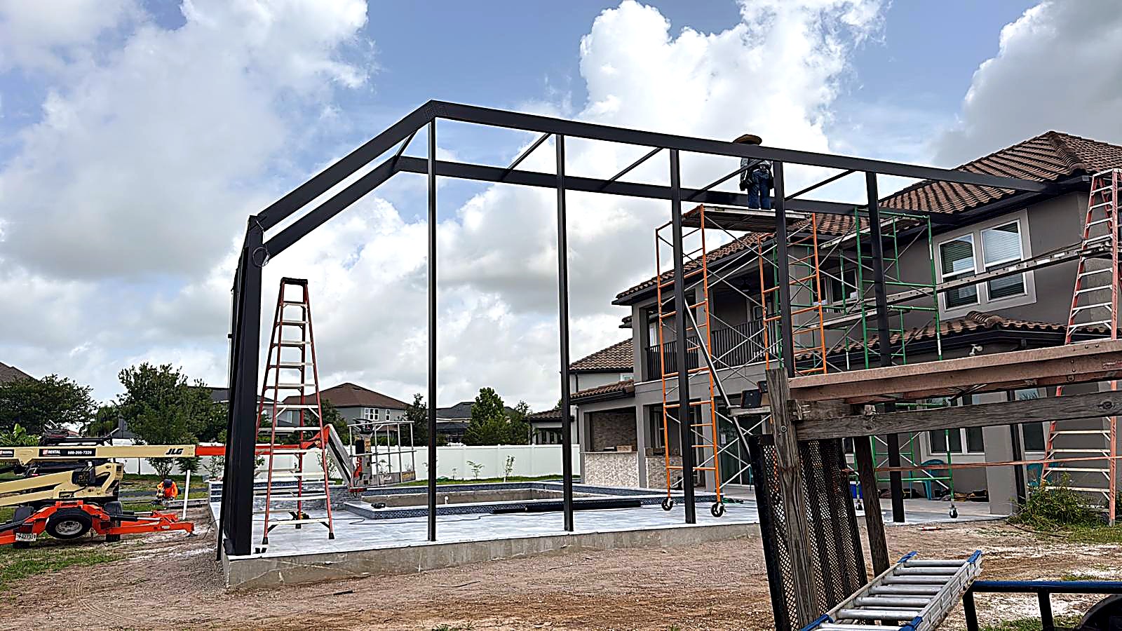 Steel-frame pool cage skeleton under construction behind a tan two-story tile-roof home in Land O’Lakes, FL